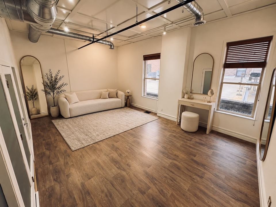 The Lounge set with a white sofa on a patterned rug, a small vanity with a stool, arched mirrors and two tall windows.