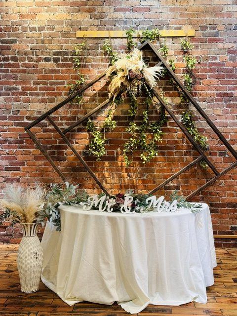 A sweetheart table with a Mr and Mrs sign under a greenery arch on the Ballroom brick wall.