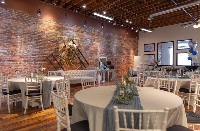 Round tables with white cloths and chiavari chairs in the Ballroom, with a sofa and arch against the brick wall.