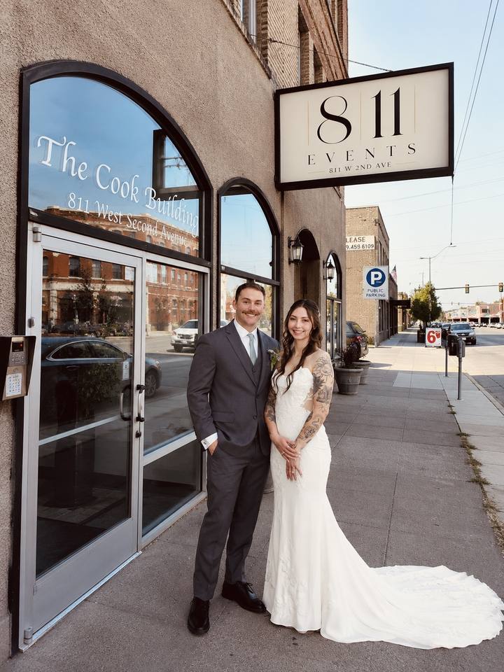 The Cook Building entrance at 811 W 2nd Ave: an arched glass door and windows lettered The Cook Building, under a hanging 811 Events sign, with a couple standing in front of the door.