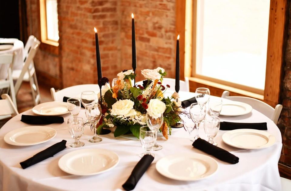 A round table in the Loft with black taper candles, white roses and black napkins.
