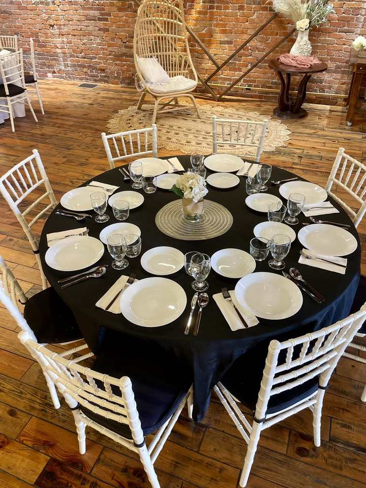 The Business set-up: a round table in a black cloth with porcelain plates, goblets, silverware and a small floral centerpiece.