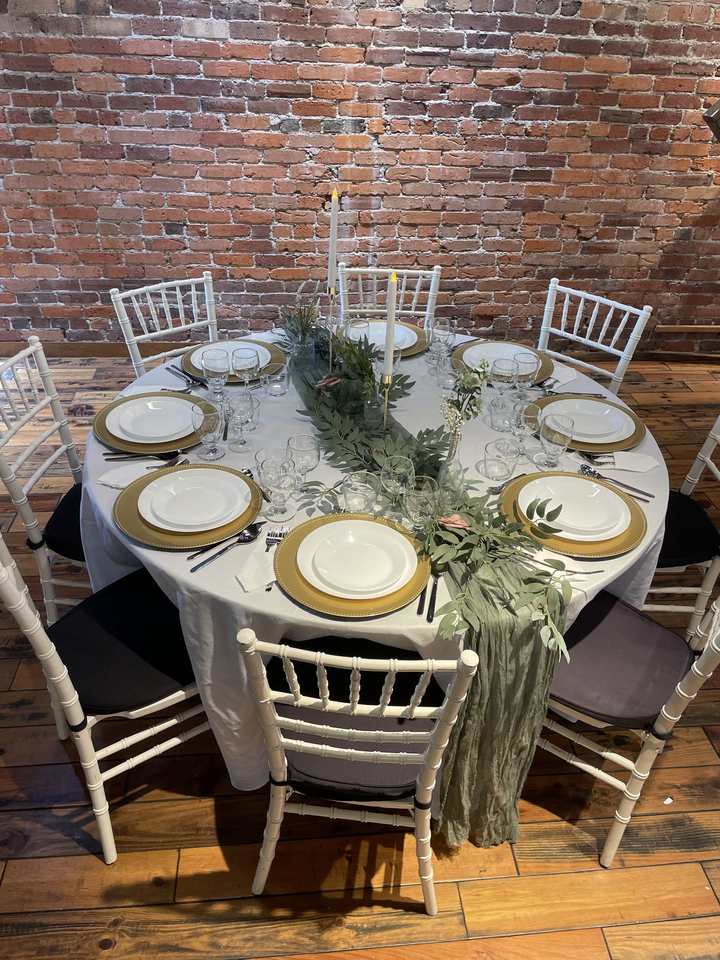 The Elegant set-up: gold chargers, wine glasses, taper candles and a greenery runner on a round table against the brick wall.